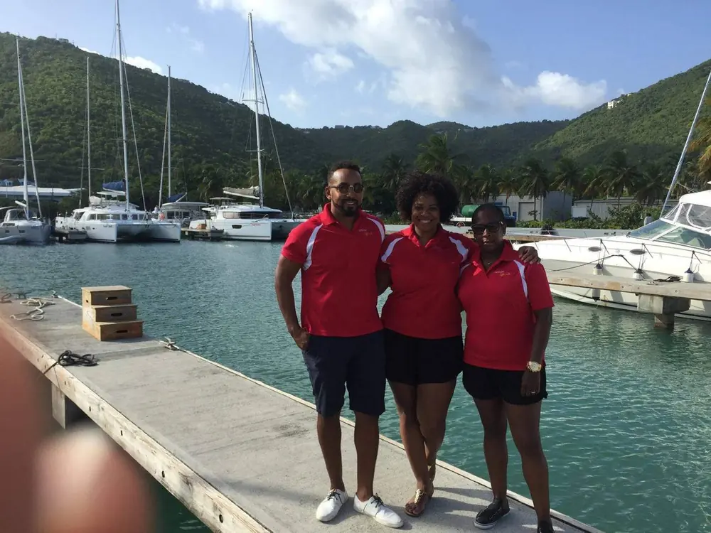 Three travelers in matching red shirts on a marina dock in the islands